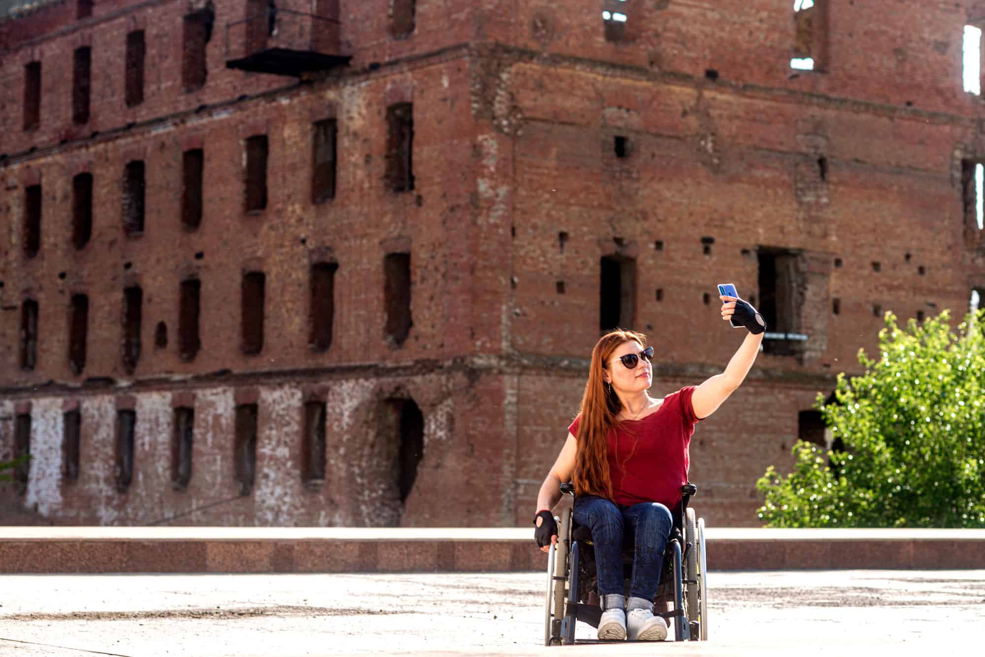 A young person seated in a wheelchair takes a picture of themself in front of a historical monument.