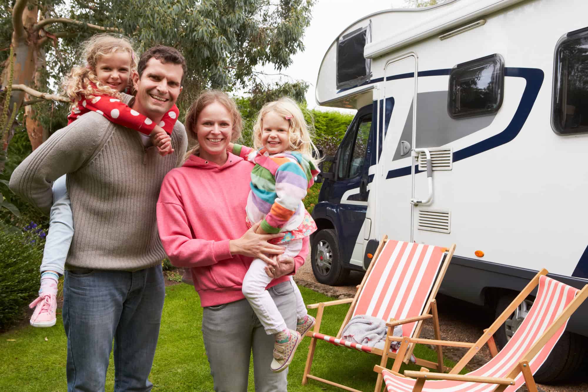 A smiling family poses outside of their RV.
